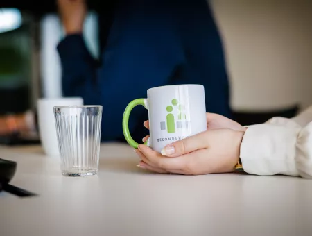 One hand holds a white cup with a green logo on it